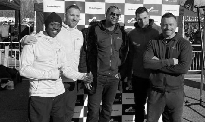 Careers picture A group of five men posing in front of a branded event backdrop, smiling and celebrating their participation in a sports or fitness event.
